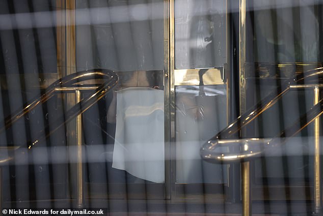 A worker can be seen sticking tape to the glass frontage of the Canary Wharf hotel today