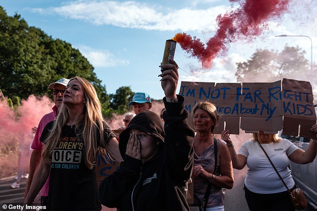 Protesters hold up red smoke cannisters and signs outside the hotel in Epping