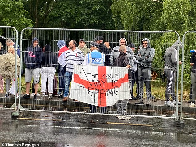 A police officer watches over protestors in front of an English flag reading 'The Only Way is Epping'