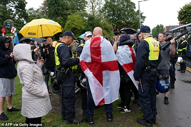 Protesters wrapped in English flags speak to police at one of the designated protest areas outside The Bell Hotel