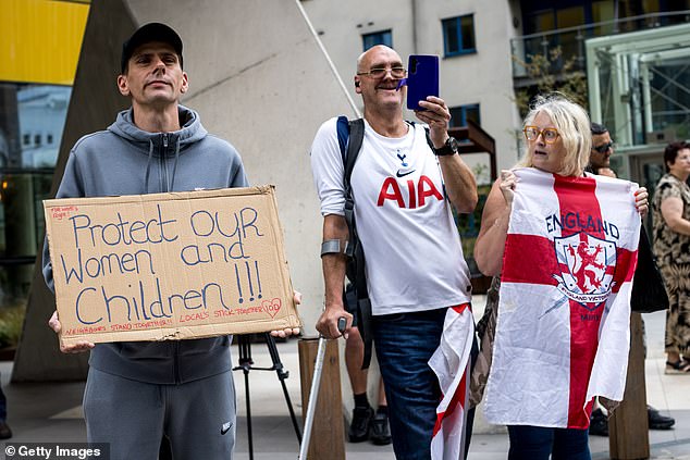 A man holds a placard and looks on from the other side of the street as protesters attend a rally organised by Stand Up To Racism outside the Britannia International Hotel