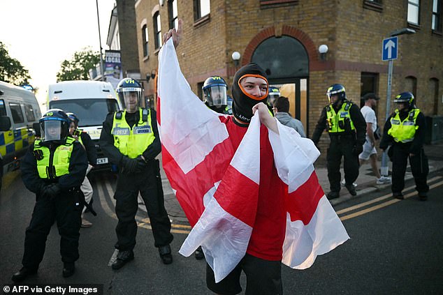 A protester wrapped in the St George's flag stands in front of a line of riot police in Epping
