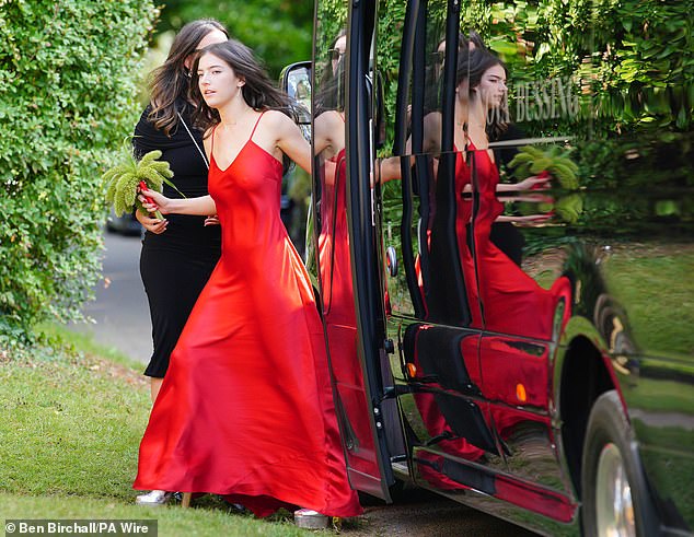 Another bridesmaid wearing a stunning red satin gown arrives at the church holding posies made of ferns