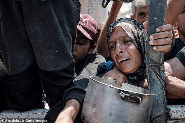 Palestinians wait in queue to get hot meals distributed by aid organizations in Gaza City, Gaza on July 26, 2025