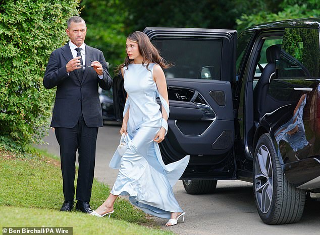 A wedding attendee arrives in a chic baby blue satin gown with white heels and a white handbag