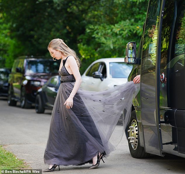 A guest wearing a grey dress wrapped in tulle heads into the Cotswolds church this evening