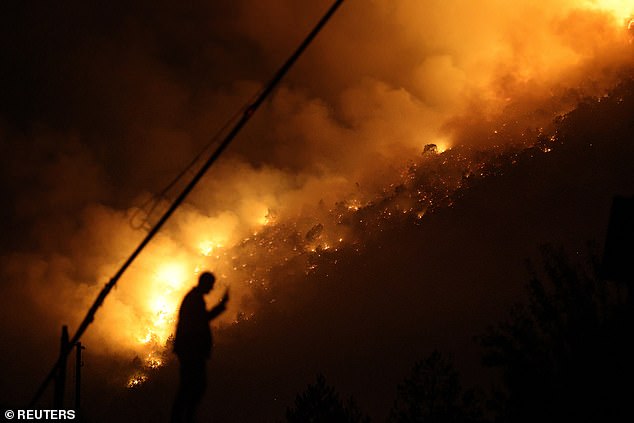 A member of emergency services stands next to a wildfire near Bulqiza, Albania