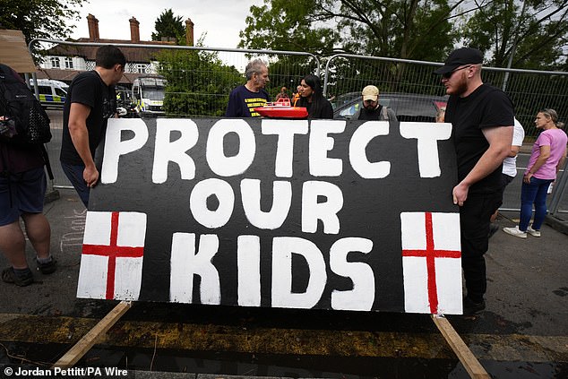 Locals hold up a sign which says 'protect our kids' after a schoolgirl was allegedly sexually assaulted by a migrant