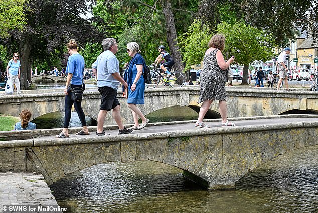 People walk across an old bridge in the picturesque village on July 17