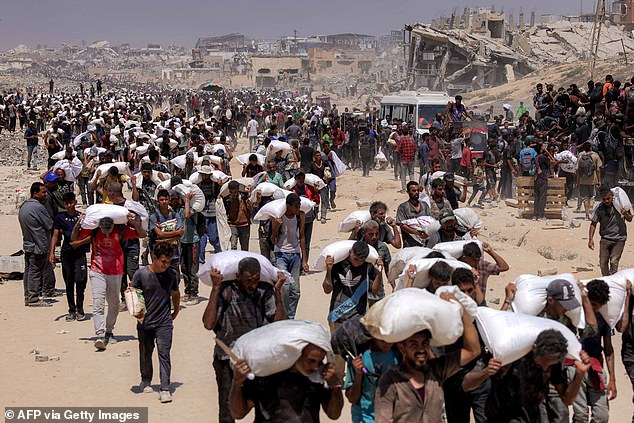People walk with sacks of flour delivered after trucks carrying humanitarian aid entered northern Gaza on July 27