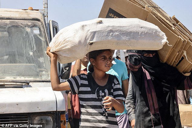 A Palestinian girl carries a bag of food aid as a woman transports empty cardboard boxes on her shoulder in the al-Mawasi camp in Rafah in the southern Gaza Strip