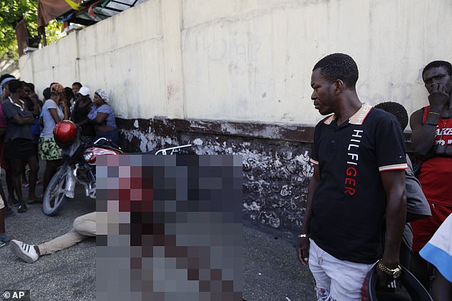 Residents watch on as a man lays dead in a pool of blood on the street