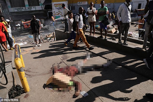 People walk past the body of a man shot dead in the morning of March 18, 2024 in Port-au-Prince