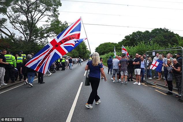Across the High Road, residents demanding the hotel's closure were gathering (pictured), some draped in Union Jacks, others waving St George's Crosses