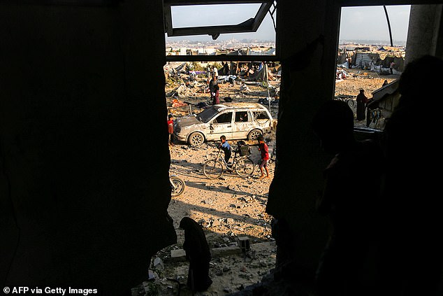 A boy pushes a bicycle near a destroyed vehicle and tents sheltering displaced people as pictured through the remains of a damaged building in the southern Gaza Strip on July 28