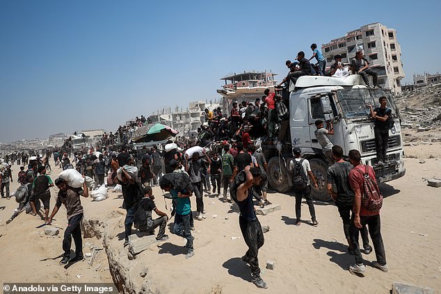 Palestinians carry sacks of flour distributed from aid trucks in the coastal Zikim area of northern Gaza, as they walk away from the distribution point under harsh conditions on July 27
