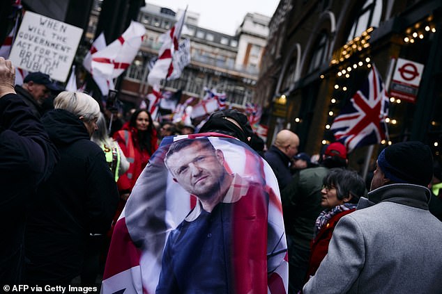 A supporter of Tommy Robinson wears a flag picturing him on his back