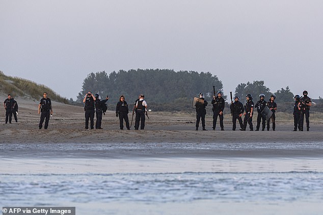 The group of cops were decked out in full riot gear including helmets, shields and batons as they stood to watch people board a smuggler's inflatable dinghy on Gravelines beach