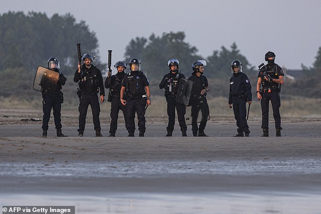 French police officers stand on Gravelines beach as migrants board a smuggler's inflatable dinghy on Tuesday
