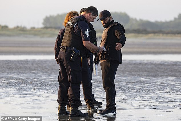 French police officers inspect a migrant trying to board a smuggler's inflatable dinghy off the coast of Gravelines earlier today