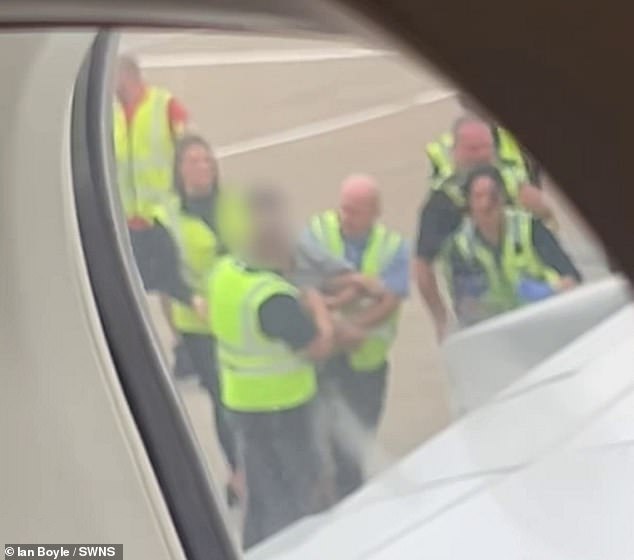Multiple airport staff are required to escort the two men, both dressed in casual clothing, away from the runway separately