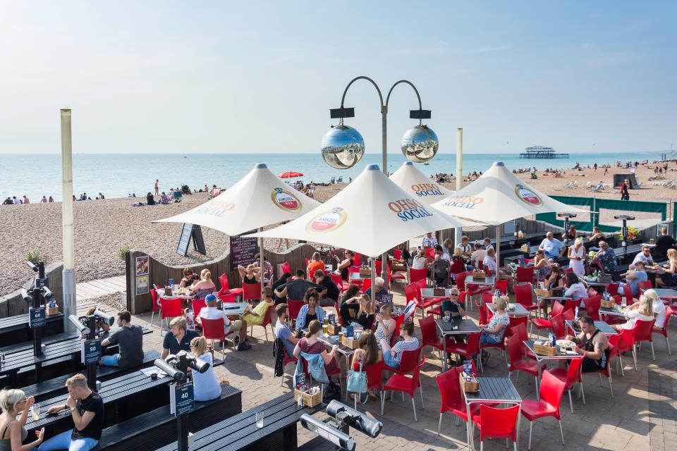 Beach bar with many patrons seated at red tables.