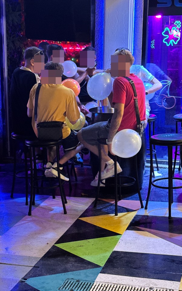 People inhaling nitrous oxide from balloons at a bar.