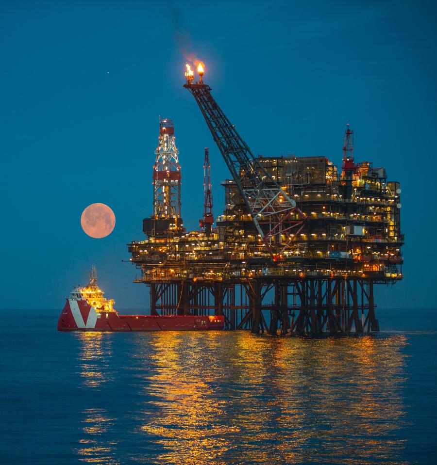 Oil platform at night with a large moon and a ship.