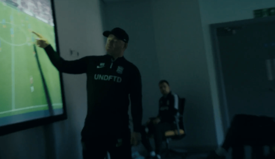 A coach points at a soccer strategy displayed on a screen.
