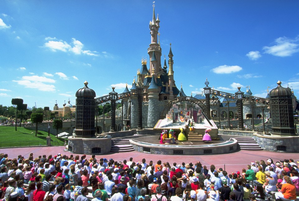 A large crowd watching a performance in front of Sleeping Beauty Castle at Disneyland Paris.