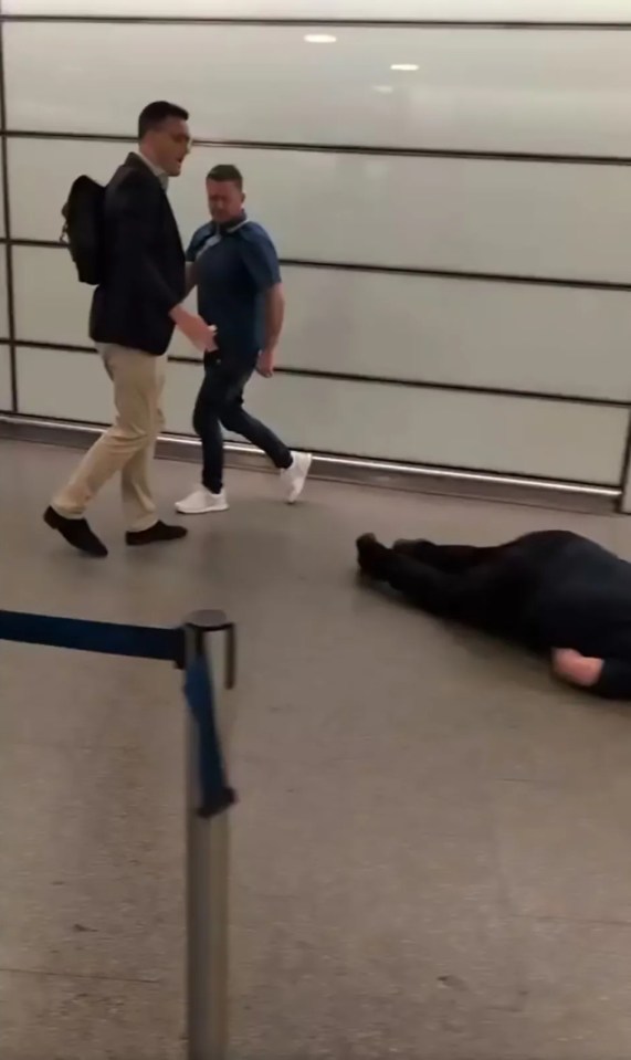 A man lying on the ground at a train station while two men walk away.