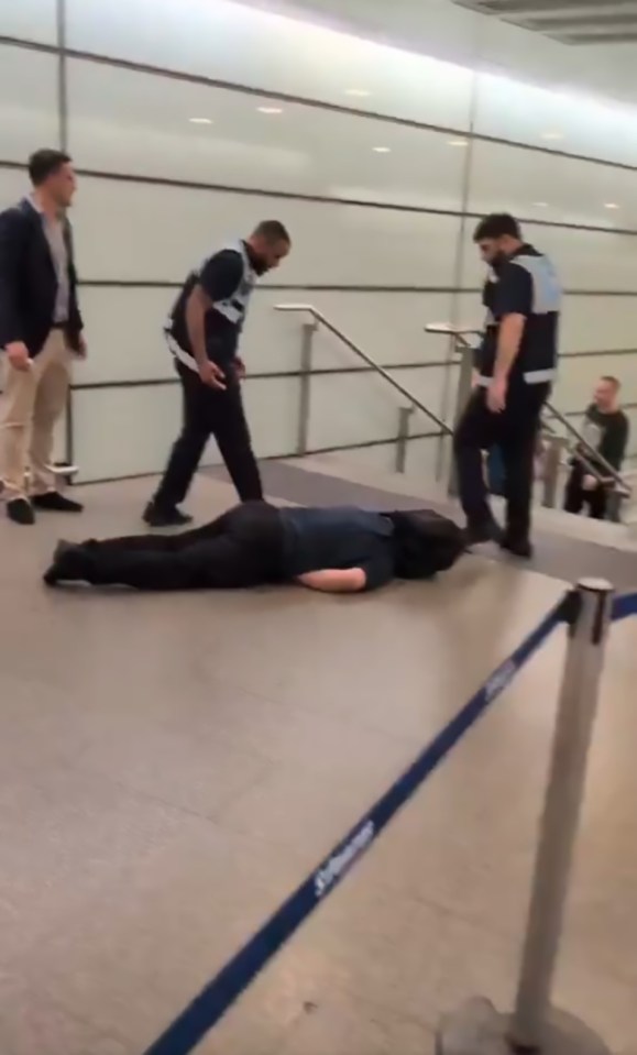 Person lying on the floor at a train station with security personnel nearby.