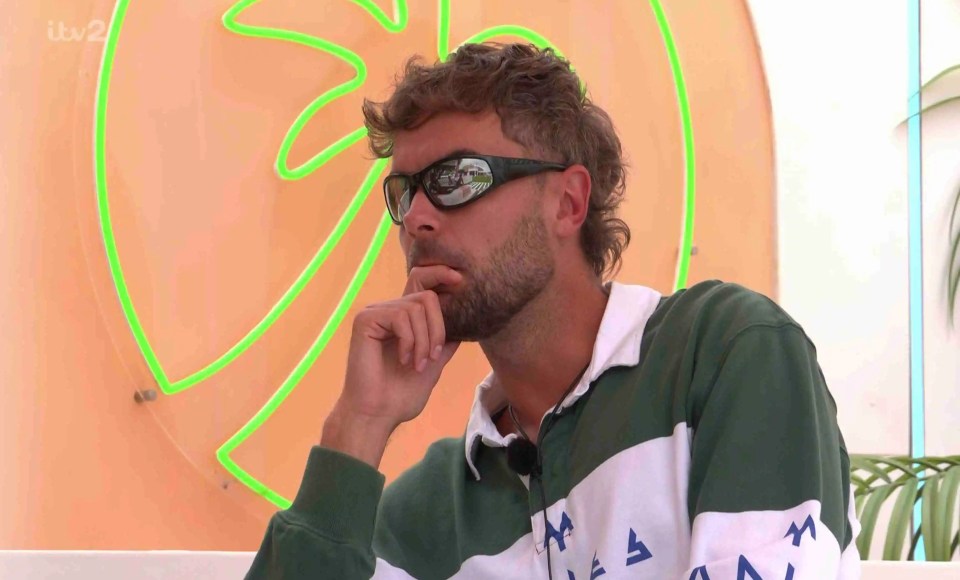 Man wearing sunglasses and a rugby shirt, deep in thought.