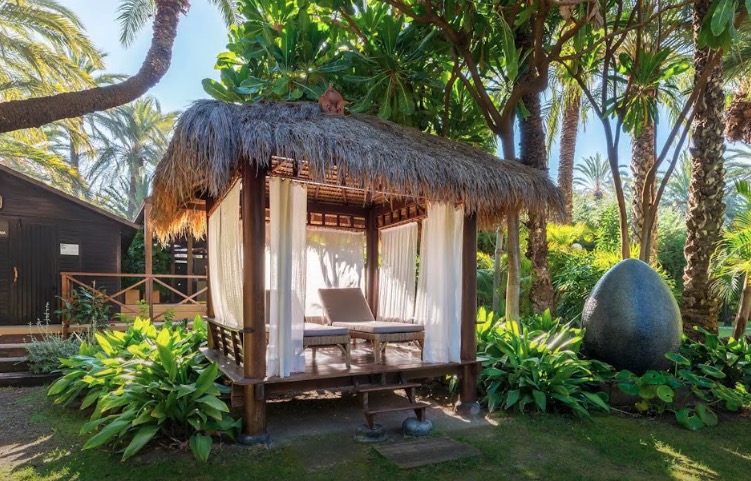 Relaxation area with thatched roof gazebo and lounge chairs in a tropical garden.