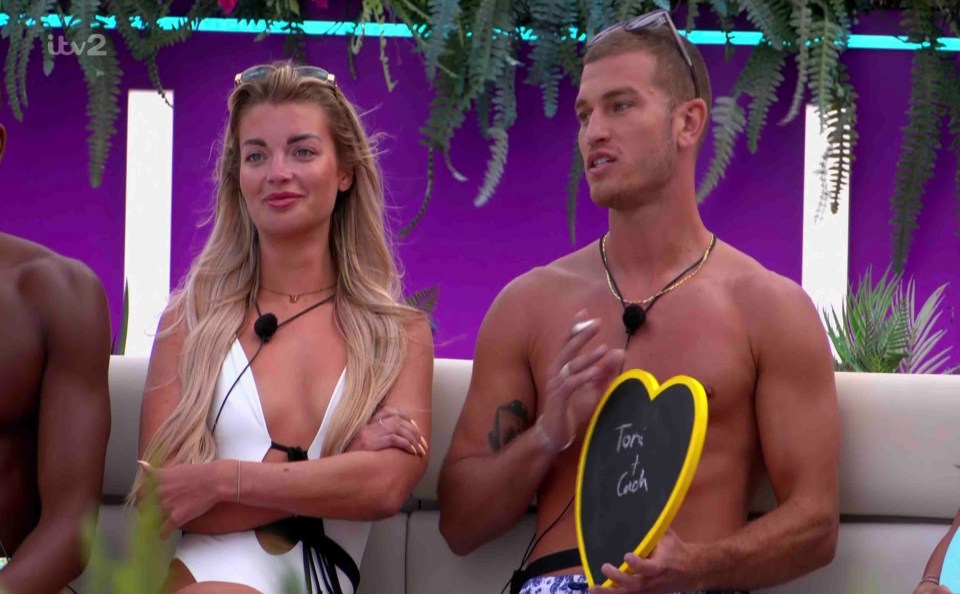 Love Island contestants Toni and Cach holding a heart-shaped chalkboard.