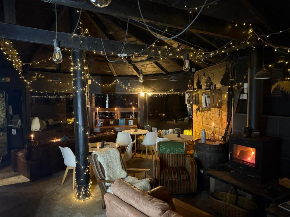 Cozy bar interior with string lights, a wood-burning stove, and comfortable seating.