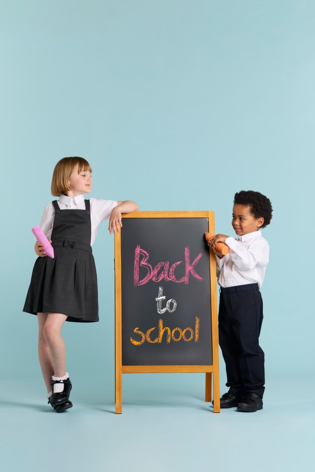 Two children in school uniforms stand on either side of a chalkboard that says "Back to School."