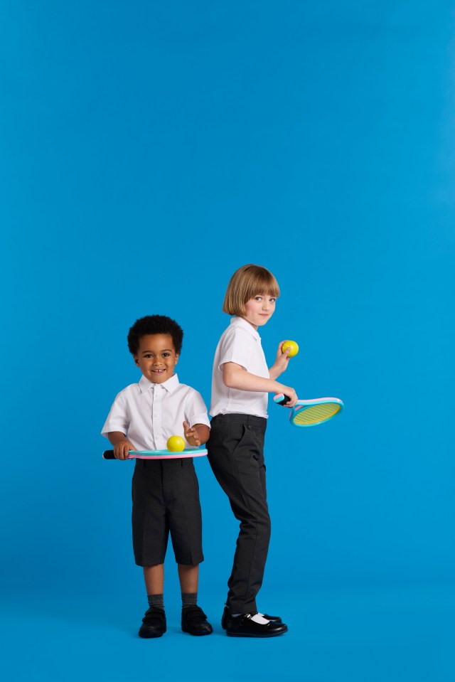 Two children in school uniforms playing tennis.