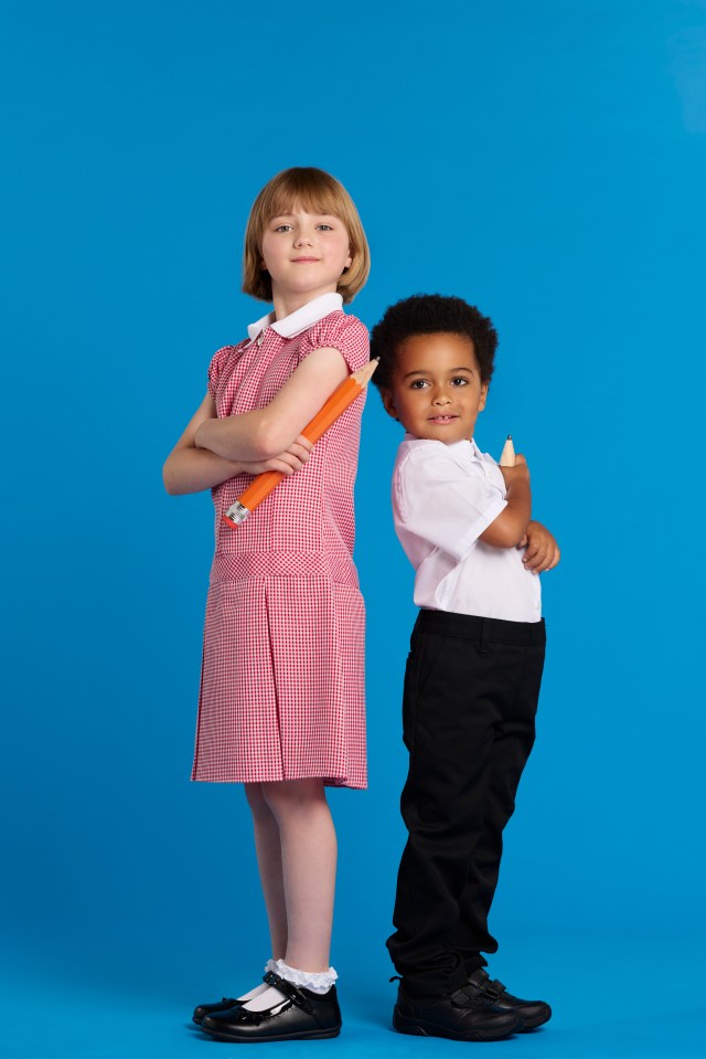 Two children in school uniforms stand back-to-back holding large pencils.