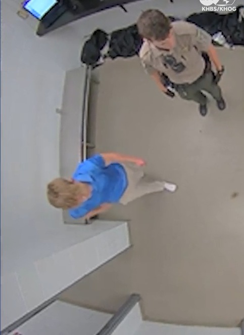 Surveillance footage of a person in custody being escorted by an officer.