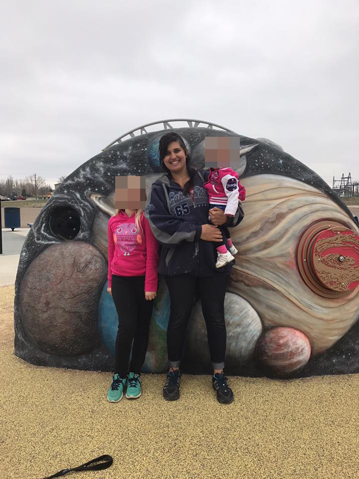 Woman and two children posing in front of a playground mural.