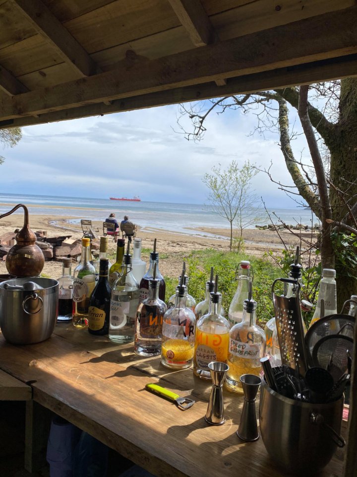 Outdoor bar with ocean view, featuring various liquor bottles and cocktail equipment.
