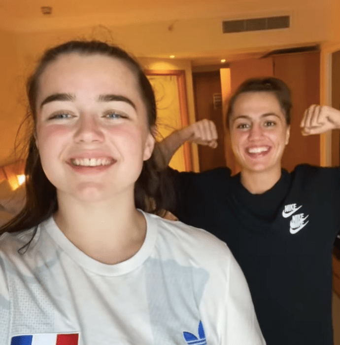 Two women flexing their biceps in a hotel room.