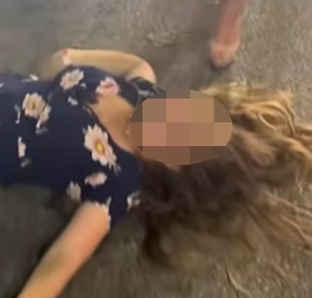 A woman in a black dress rushes to his aid, but is attacked by the crowd, suffering two blows to the face. The impact caused her to fall, with her head slamming the pavement. She became unconscious as blood spewed from her mouth