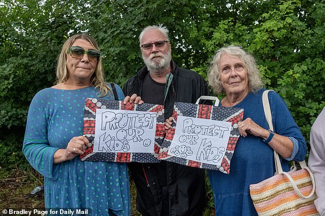 Three protesters hold signs reading 'Protect our kids'