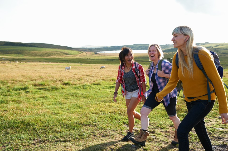Three women hiking and laughing in a field.
