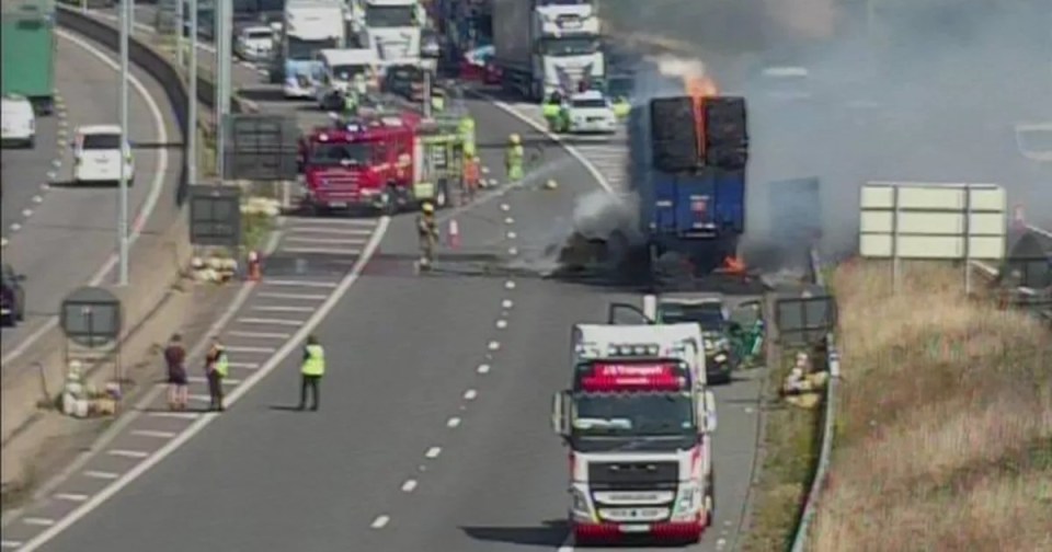 Burning lorry on highway with emergency responders.