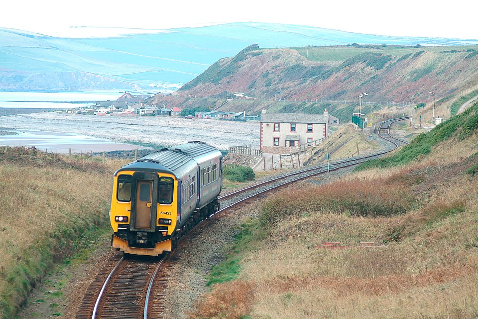 Train on coastal railway line near houses and mountains.