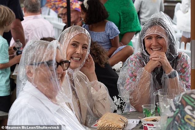 Racegoers smile despite torrential rain at Royal Windsor Racecourse in Berkshire yesterday