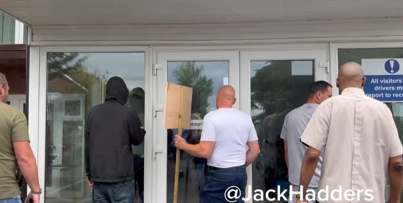People standing outside a building with a wooden sign.
